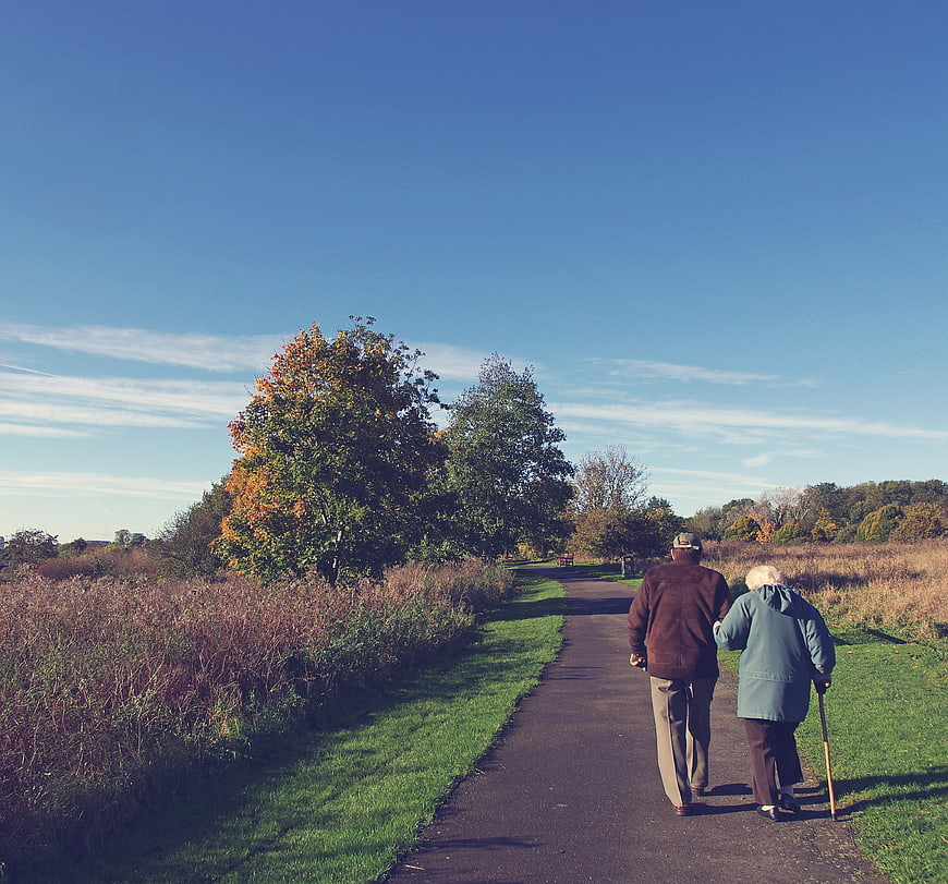 Senior couple walking away on park path in autumn