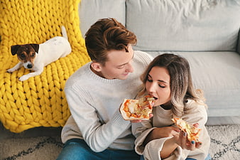 Young couple eating pizza on floor with dog