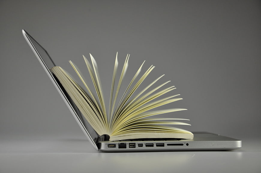 Open book emerging from laptop screen on gray background