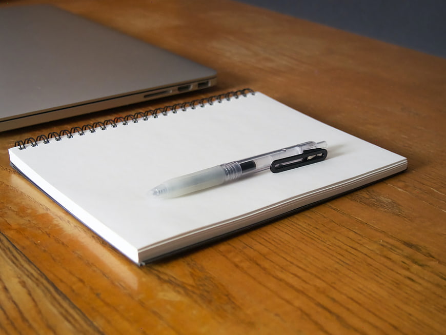 Blank Notebook and Pen on Wooden Desk with Laptop
