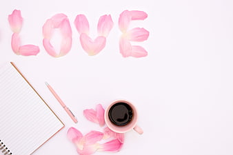 Pink flower petals spelling LOVE with coffee and notebook