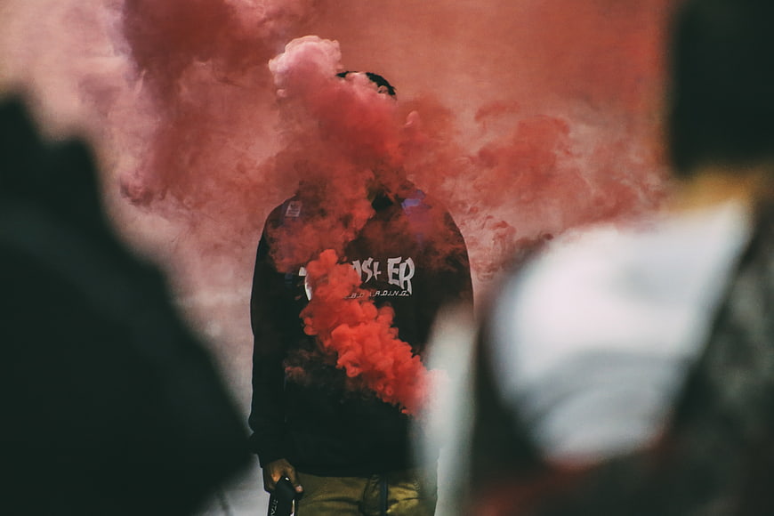 Man holding red smoke grenade in dark atmosphere