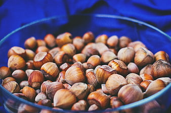 Close-up of Hazelnuts in a Glass Bowl on Blue Background