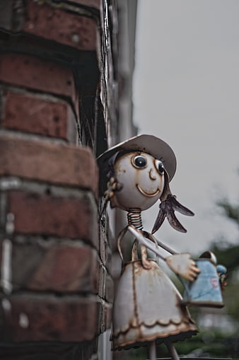 Rusty metal girl figurine holding watering can on brick wall