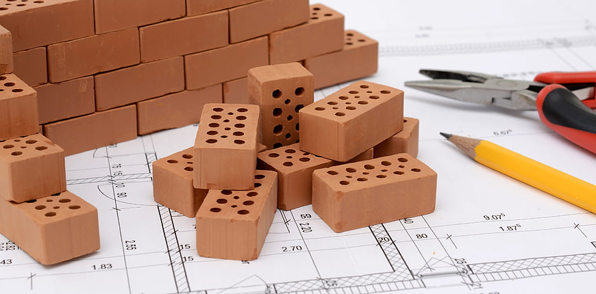 Miniature clay bricks and architectural blueprints with tools