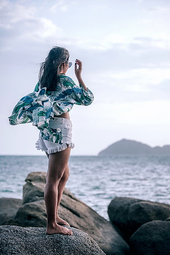 Barefoot woman in tropical shirt standing on coastal rocks