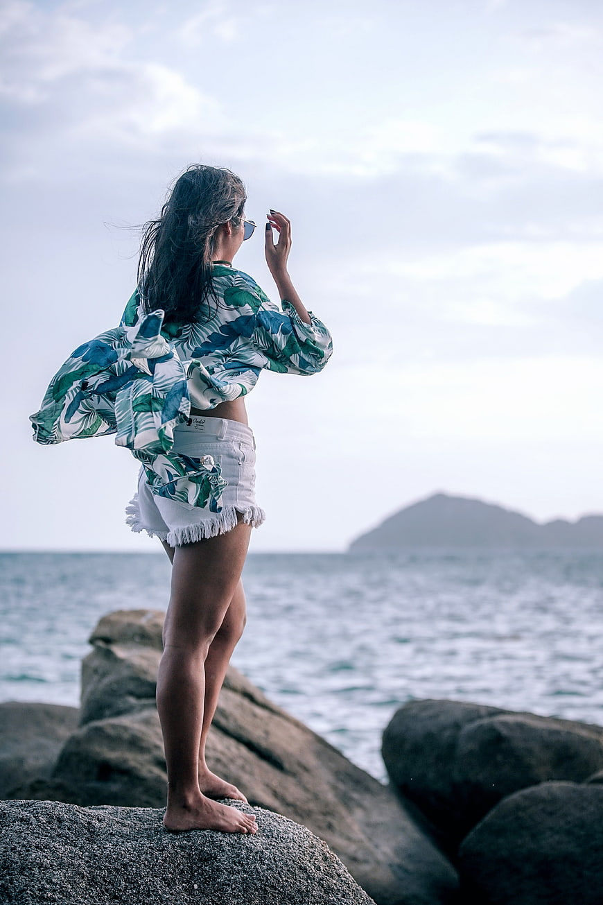 Barefoot woman in tropical shirt standing on coastal rocks