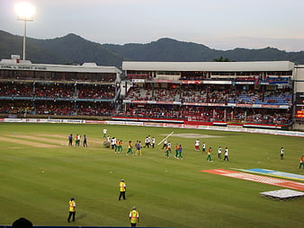 Cricket match preparation at stadium with crowd and mountains