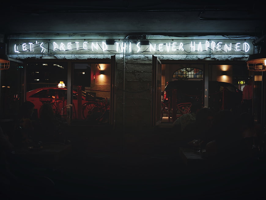 Neon sign reading let's pretend this never happened at night