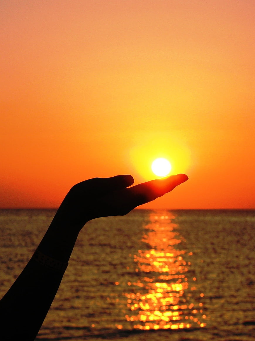 Silhouette of hand holding sun over ocean sunset