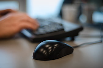 Close-up of black computer mouse on office desk with blurred typing hands