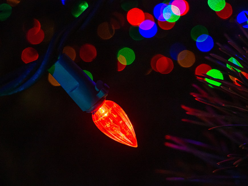 Close-up of glowing red Christmas light bulb with colorful bokeh