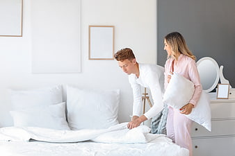 Happy young couple making bed in bright modern bedroom