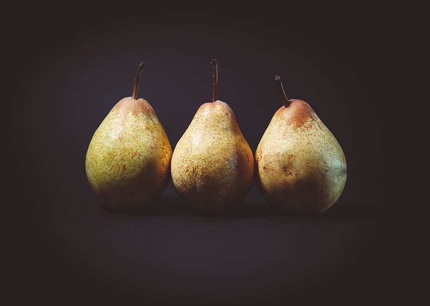 Three ripe pears in a row on a dark background