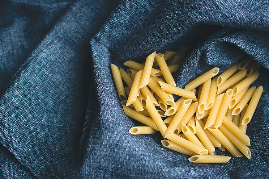 Uncooked penne pasta on blue linen background