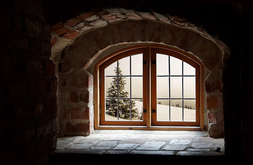 Arched wooden window looking out onto a snowy winter landscape