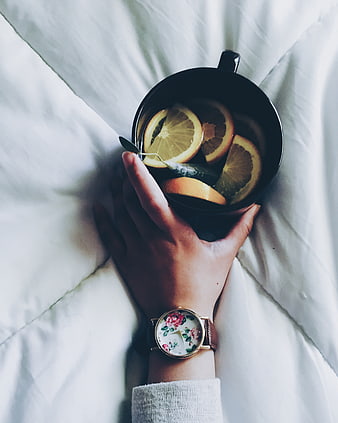 Hand holding black mug with citrus tea on white bed