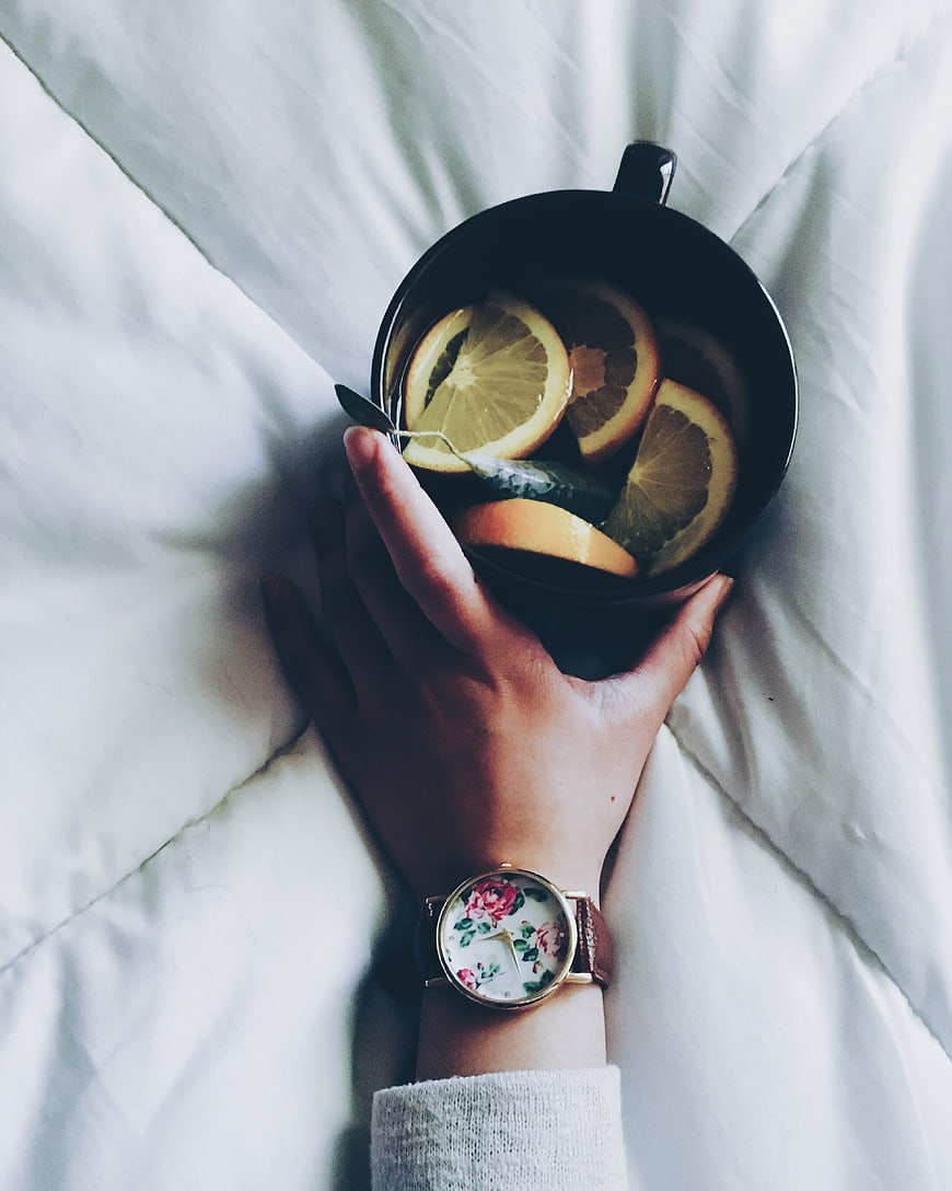Hand holding black mug with citrus tea on white bed