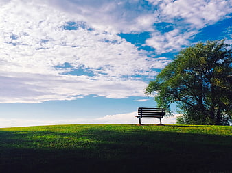Lone wooden bench on a grassy hill under a dramatic cloudy blue sky