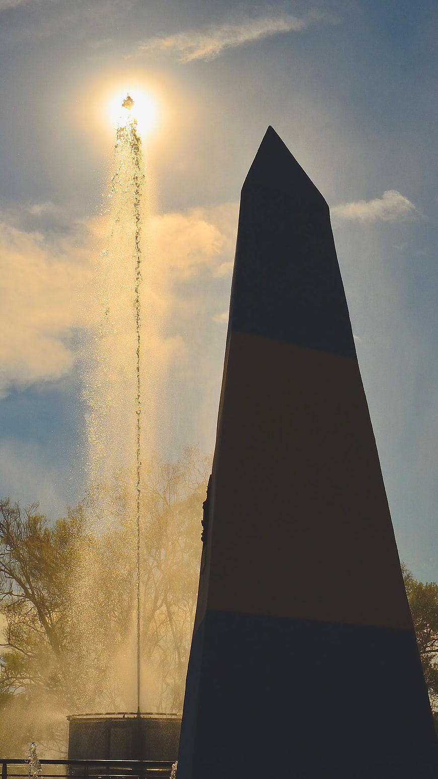 Black Obelisk Monument Backlit by Sun and Fountain Spray