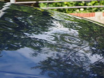 Close-up of hail damage on a car roof with rain ripples