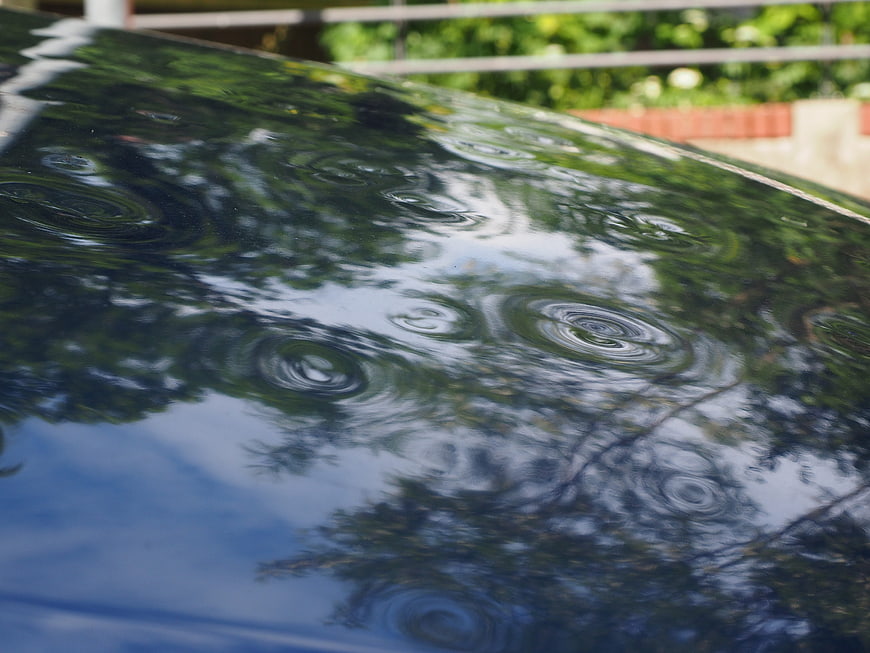 Close-up of hail damage on a car roof with rain ripples