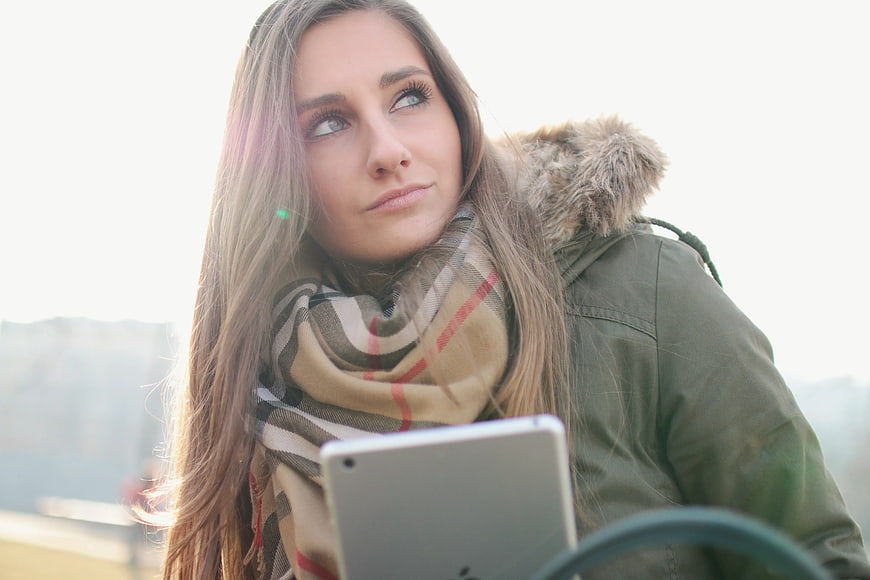 Woman in Winter Coat Looking Up with Tablet