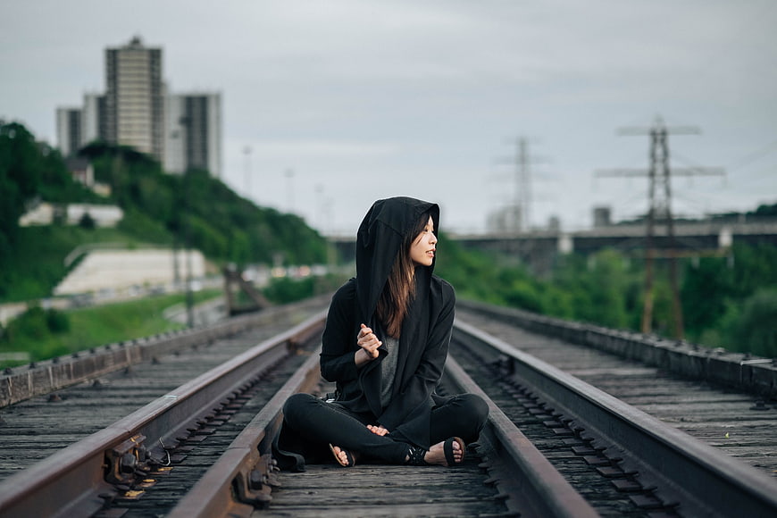 Woman in black hoodie sitting on railroad tracks in urban landscape
