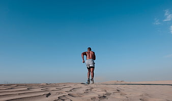 Athletic Man Running on Sand Dunes Under Blue Sky