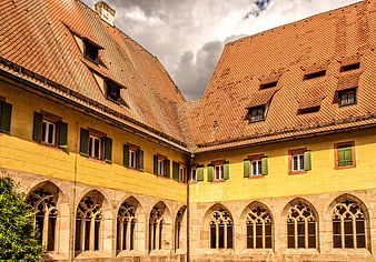 Historic yellow monastery courtyard with Gothic arches and tiled roof
