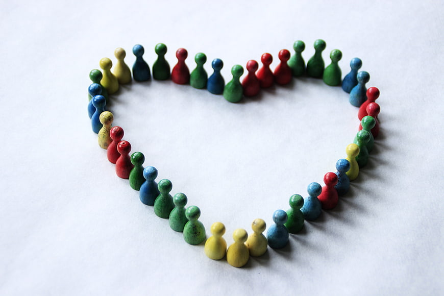 Colorful Wooden People Figurines Arranged in Heart Shape on White Background