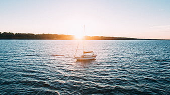 Lone Sailboat on Calm Ocean at Golden Sunset
