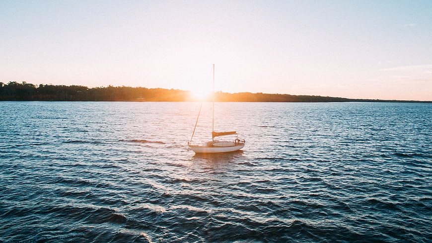 Lone Sailboat on Calm Ocean at Golden Sunset