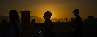 Silhouettes of three people watching sunset over city skyline