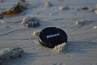 Black Nikon lens cap resting on sandy beach