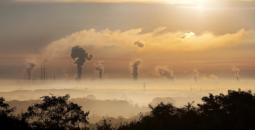 Industrial smokestacks emitting pollution into hazy sunset sky