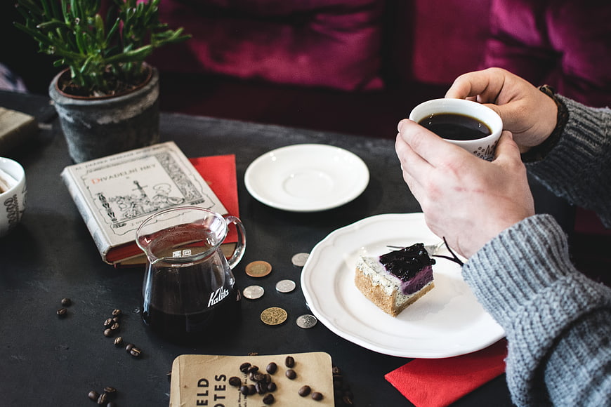 Hands holding coffee cup with blueberry cheesecake on table