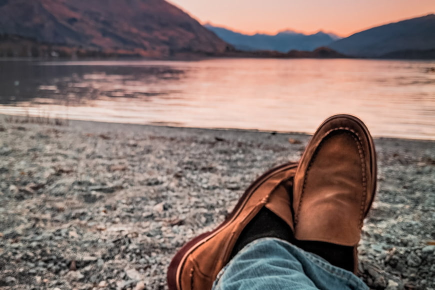 Relaxed Man's Feet in Brown Boots by Lake at Sunset