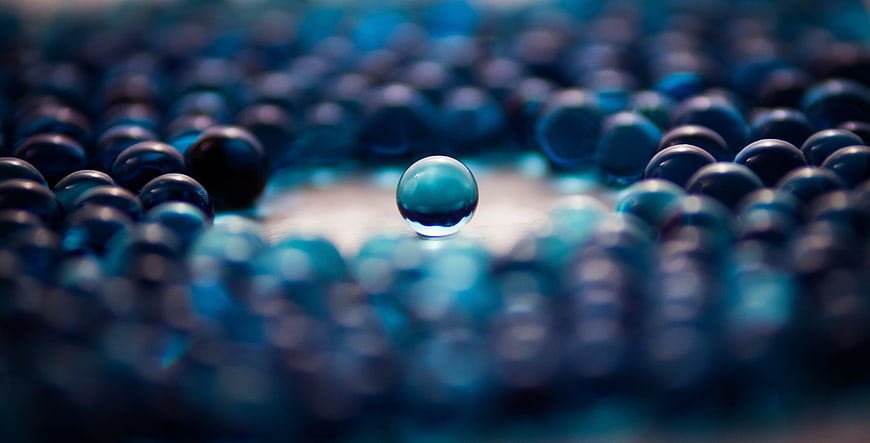 Blue glass marble standing alone in a crowd of spheres