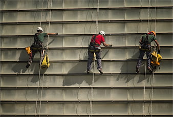 Three industrial rope access workers cleaning a large building facade