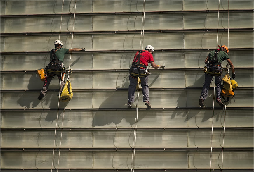 Three industrial rope access workers cleaning a large building facade