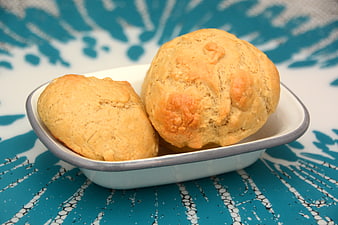 Two golden homemade bread rolls in a white dish on blue patterned background