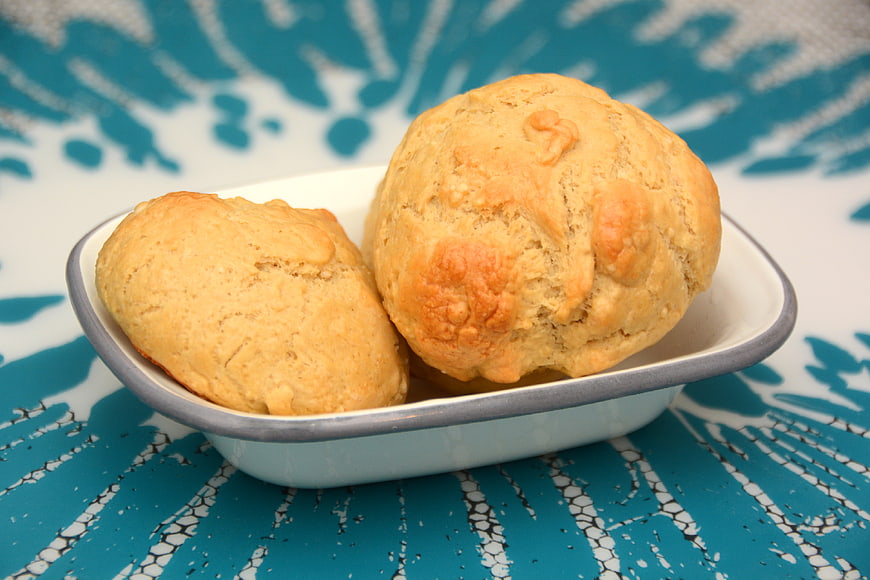 Two golden homemade bread rolls in a white dish on blue patterned background