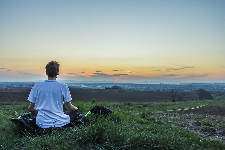 Man Meditating on Hilltop Overlooking Valley at Sunset