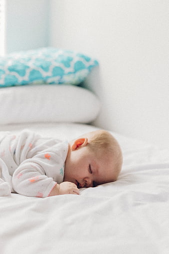 Sleeping baby on white bed with blue pillow