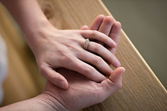 Close-up of couple's hands with engagement ring on wooden railing