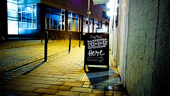 Crafted Beer Here Chalkboard Sign on Cobblestone Street at Night