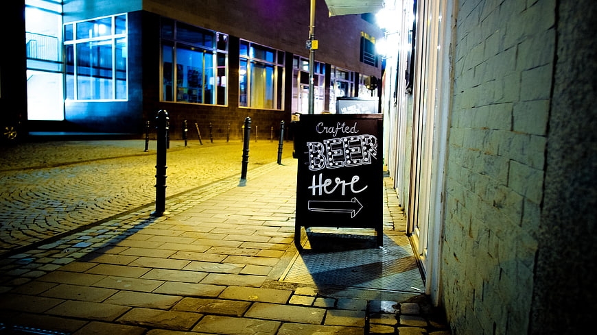 Crafted Beer Here Chalkboard Sign on Cobblestone Street at Night