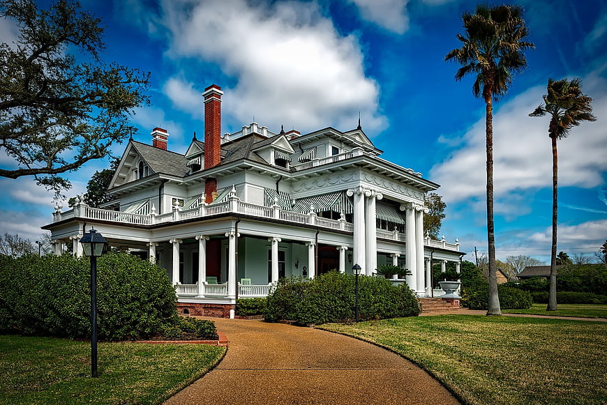 Grand white Victorian mansion with wraparound porch and palm trees