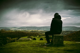 Man sitting on stone overlooking dramatic green valley landscape
